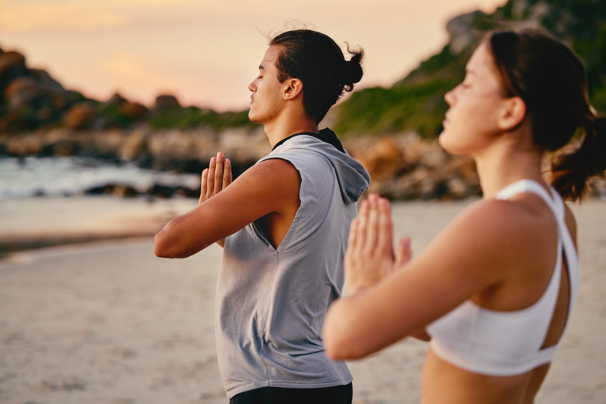 Couple, prayer hands and yoga meditation at beach outdoors for health and wellness. Sunset, pilates
